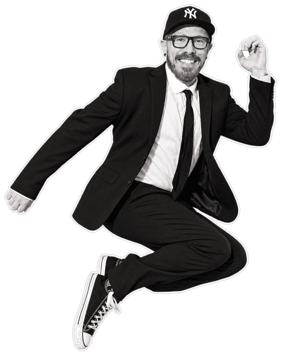 Jason Donnelly, mid-jump in a black suit, tie, NY cap and Converse, cut out against black.